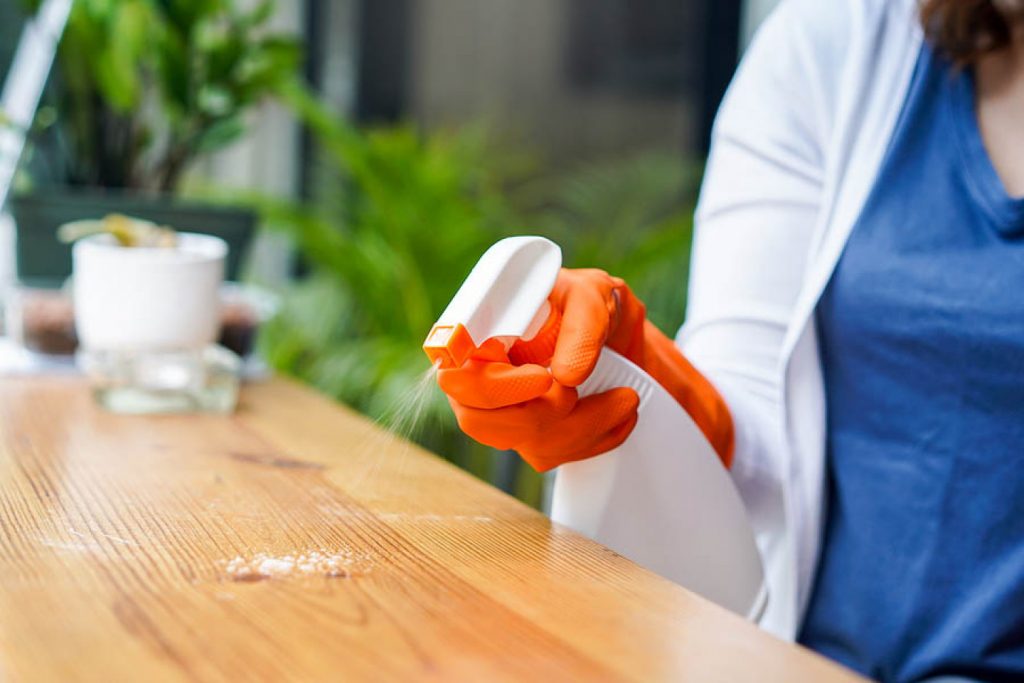 House Cleaner outside cleaning a table with a spray cleaning product