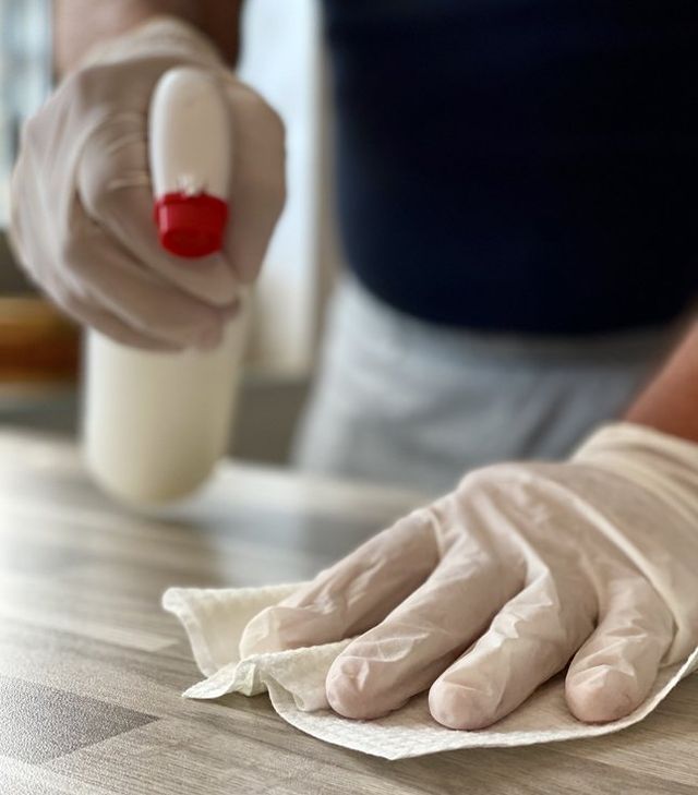 House cleaner with gloves on using sanitizer to clean table